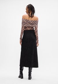 Top off-shoulder em xadrez transparente marrom, combinado com uma saia longa preta com um padrão texturizado. Botas pretas até o joelho completam o look.