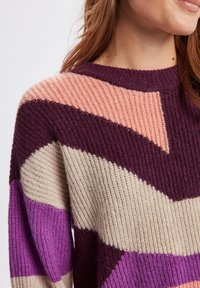 Maglione lavorato a maglia con una texture a coste, con motivi in viola scuro, rosa chiaro, beige e viola. Collo rotondo e spalle scese.