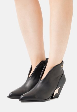 Zwarte leren enkellaarzen met een spitse neus, featuring een uitgesneden ontwerp en een unieke sterrenvoet. Gladde textuur met gouden accenten.