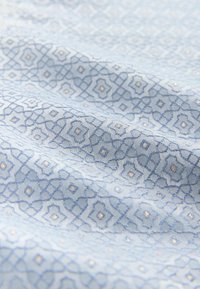 Textilstoff in Hellblau mit geometrischen Mustern in Dunkelblau und goldenen Akzenten, mit glatter Textur und dezentem Glanz.