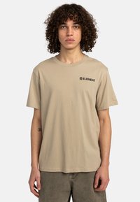 Camiseta de algodón beige con mangas cortas, que presenta un logo negro de "ELEMENT" en el pecho. Diseño sencillo, ajuste relajado, cuello redondo clásico.