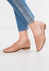 Chaussures en cuir beige clair avec un design à bout pointu et un talon en bois bas. Portées avec un jean bleu cropped, effiloché et ayant un lavage clair.