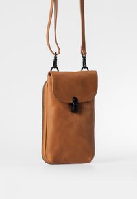 Kleine hellbraune Leder-Umhängetasche mit Klappe, schwarzem Verschluss, Reißverschlüssen an den Seiten und verstellbarem Riemen vor weißem Hintergrund.