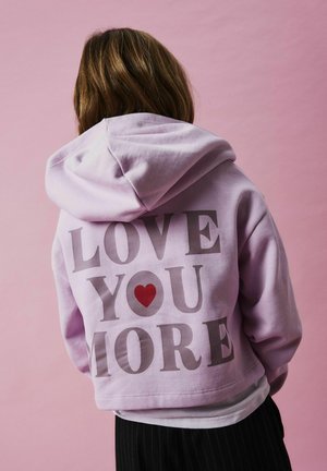 Lila Kapuzenpulli mit einem cropped Design. Auf dem Rücken steht der Text "LOVE YOU MORE" in Grau, begleitet von einem roten Herzakzent. Weicher Stoff.