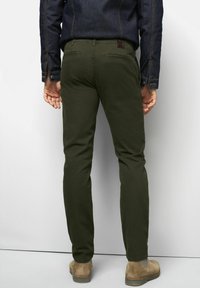 Olijfgroene broeken met een slim fit ontwerp, gemaakt van zachte stof. Voorzien van achterzakken, een leren patch in bruin, en gecombineerd met tan schoenen.