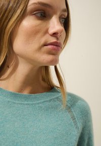 Pull en cachemire bleu clair avec un col rond et des manches raglan, présentant une texture subtile et des détails de couture délicats.