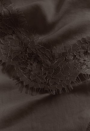 Tela oscura con delicado ribete de encaje floral que presenta malla fina y bordes con flecos, dispuesta con suaves pliegues y sombras.