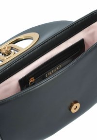 Borsa a mano in pelle nera con una chiusura circolare dorata, dotata di un morbido rivestimento rosa e una tasca con zip all'interno. Texture liscia, design elegante.