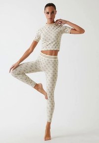 Beige gemustertes, kurz geschnittenes Oberteil und passende Leggings, beide mit geripptem Saum. Das Material wirkt weich; die Leggings haben ein dezentes geometrisches Muster.