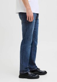 Vaqueros ajustados de mezclilla azul con lavado desteñido, costuras en contraste y diseño de pierna recta. Combinados con zapatos negros con cordones.