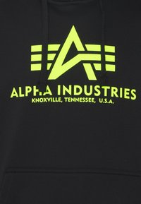 Sudadera negra con un brillante logo de Alpha Industries en amarillo y texto que dice "Knoxville, Tennessee, EE. UU." en el área del pecho.