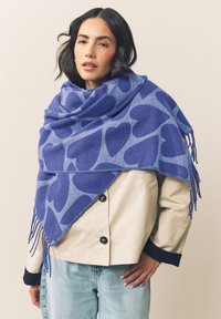 Sciarpa blu con grandi motivi a cuore, realizzata in materiale morbido, rifinita con delicati frange lungo i bordi. Si drappeggia elegantemente.