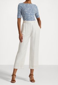 Blå blommönstrad tajt topp med korta ärmar, kombinerad med vita högmidjade vida byxor och bruna sandaler med remmar.