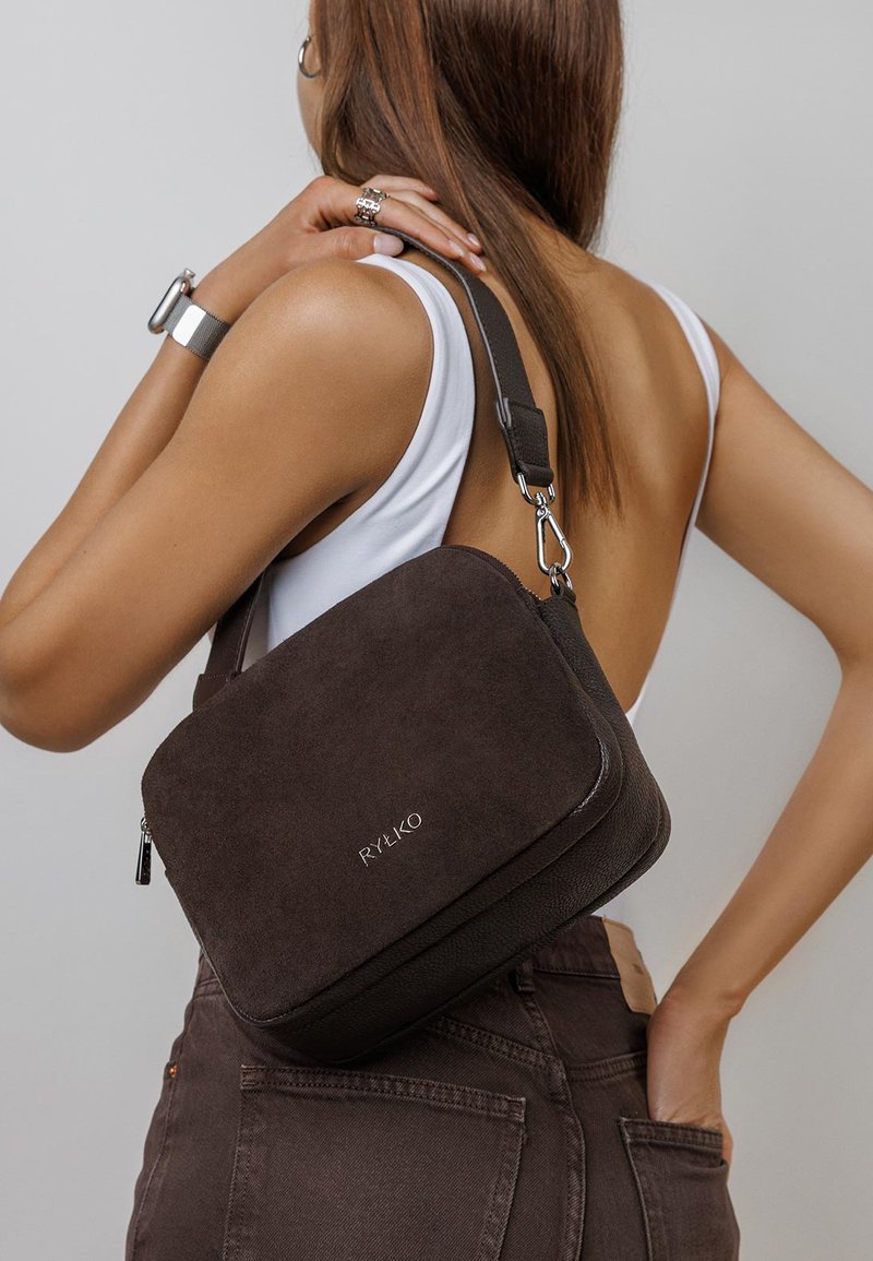 Brown suede and textured leather crossbody bag with a zip closure, adjustable strap, and silver hardware, featuring subtle branding.
