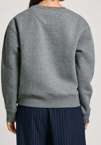 Sudadera gris con cuello redondo, puños y dobladillo acanalados. Textura suave, diseño sencillo y vista trasera sin adornos. Combinada con pantalones de rayas marino.