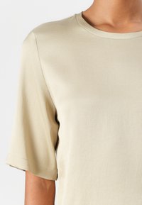Beige kortermet topp med rund halsutskjæring og mykt, glatst stoff med en lett avslappet passform. Kantene er pent sydd.
