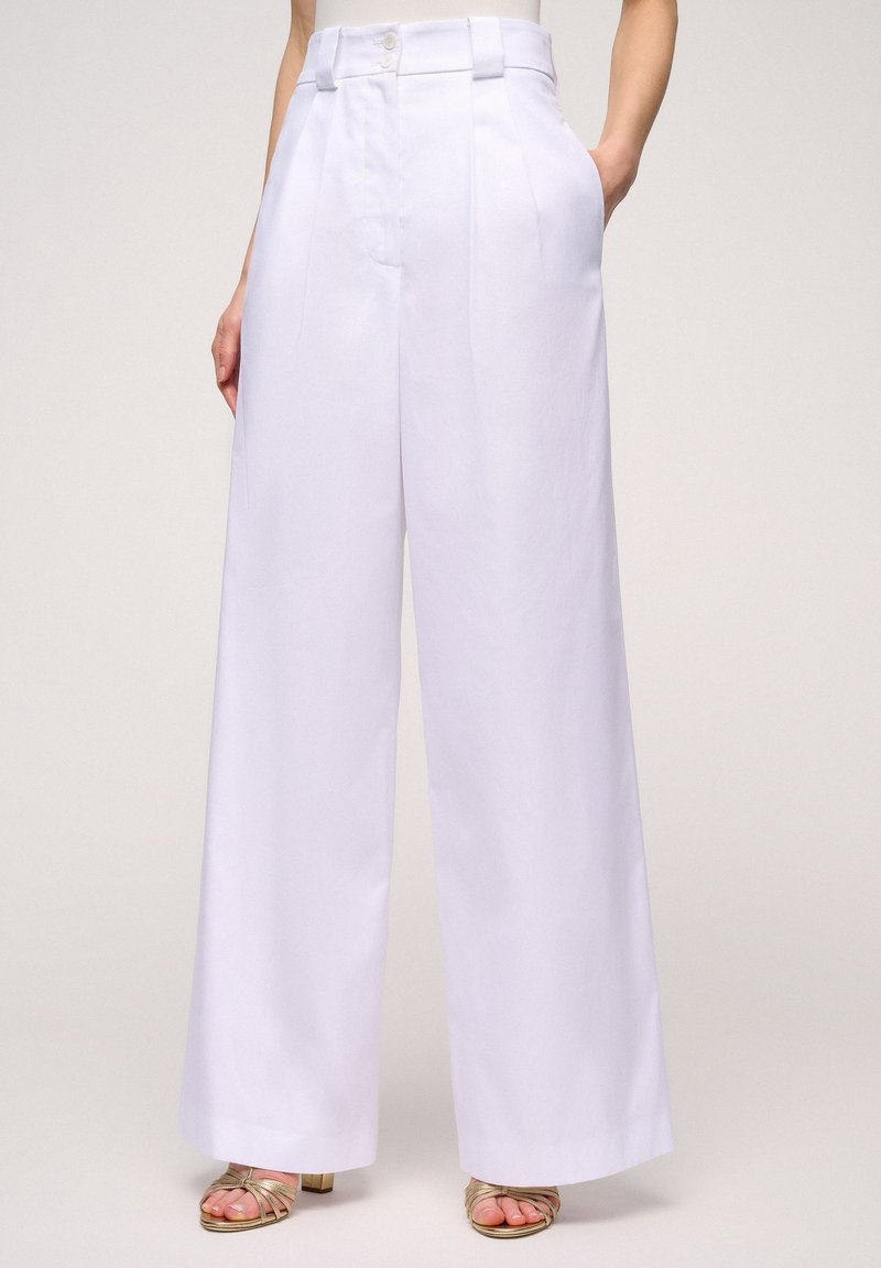 Witte wijde broek met plooien, hoge taille, twee zijzakken en een subtiele textuur. Afgewerkt met twee knopen in de taille.