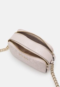 Světle růžová prošívaná crossbody taška se zlatými detaily, dvojitými zipovými oddíly a logem "GUESS" na přední straně.