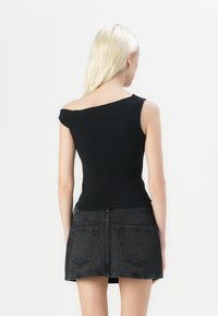 Crna off-shoulder majica s prilagođenim dizajnom i kratkim rukavima, u kombinaciji s crnom traper mini suknjom koja ima stražnje džepove i suptilnu teksturu.