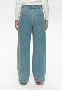 Világoskék, bő szárú farmernadrág magas derékkal, két hátsó zsebbel és nyers szegéllyel. Simább textúrájú denim anyagból készült.