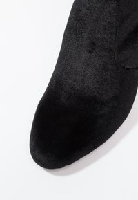 Chaussure en tissu noir et doux avec un bout pointu et un design élégant, présentant une texture lisse sans motifs ni éléments visibles.