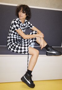 Černo-bíl dresses s kostkovaným vzorem, krátké rukávy, po kolena, kombinované s robustními černými teniskami a černými kotníkovými ponožkami.