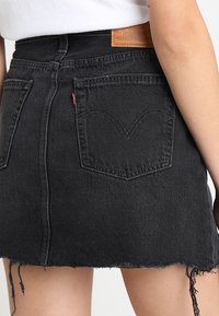 Black denim skirt with frayed hem, five-pocket design, and brand patch at the waist. Features signature stitching on back pockets.
