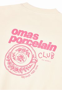Sweat-shirt crème clair avec texte graphique rose "omas porcelain CLUB" et une assiette illustrée avec un motif floral et le texte "may cause food coma".