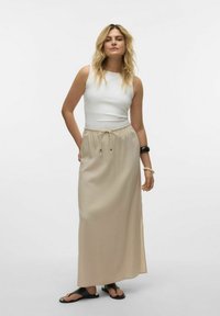 Beige maxi sukně s páskem na stažení a ozdobným kováním, spárovaná s přiléhavým bílým topem bez rukávů a černými plochými sandály.