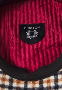 Interior matlasat cu un material roșu bogat, având un patch negru cu logo-ul "Brixton", înconjurat de un guler texturat.
