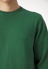 Zeleni bombažni pulover s krožnim izrezom. Ponuja subtilno vezenje logotipa "BOSS" v isti zeleni barvi. Mehak material in prilegajoča zasnova.