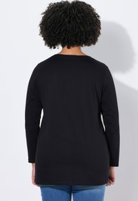 Camisa de manga larga negra con un escote redondeado, hecha de una tela suave. La camisa se combina con jeans azules, que presentan un corte relajado.