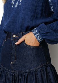 Haut texturé bleu avec des détails brodés, associé à une jupe en denim foncé avec un ourlet volanté et des surpiqûres mises en valeur.