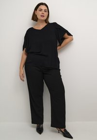 Czarny top z dekoltem w serek i luźnymi, krótkimi rękawami w połączeniu z czarnymi spodniami typu wide-leg. Model nosi czarne szpilki o spiczastym nosku, prezentując elegancki, profesjonalny wygląd.