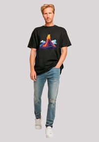 Black short-sleeve T-shirt featuring a colorful volcano graphic on the front. Worn with light blue distressed jeans and white sneakers.
