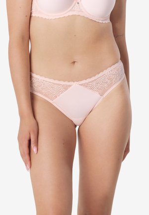 Kobieta ubrana w bladoróżowy biustonosz z koronki i satyny oraz dopasowane majtki, widoczna od połowy klatki piersiowej do górnych partii ud.