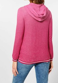 Pink hooded sweatshirt with a textured finish, featuring a white and red striped hem and cuffs, and long sleeves.