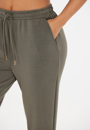 Olijfgroene joggers van zacht materiaal, met een strikband in de taille, zijzakken en een textuur voor comfort. Gouden accenten bij de veters.