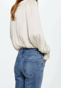 Witte, vloeiende blouse met een gerimpelde halslijn, gecombineerd met lichtblauwe, high-waisted jeans met achterzakken en een rechte pijp.