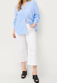 Camicia in lino azzurro chiaro con bottoni e maniche lunghe, abbinata a pantaloni bianchi a gamba larga e mule nere con tacco quadrato.