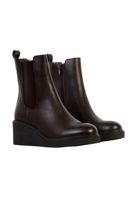 Paire de bottines compensées en cuir marron foncé avec fermeture éclair latérale et panneau élastique sur fond blanc.