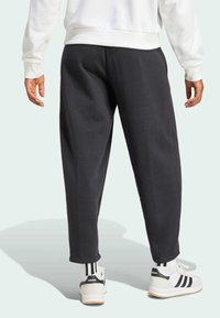Pantalons de survêtement noirs en coton avec une coupe décontractée, présentant des jambes fuselées et une texture douce, associés à des baskets Adidas blanches et noires.