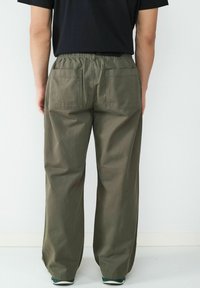 Rechtdoorlopende, olijfgroene broek met een elastische tailleband en twee grote opgestikte zakken aan de achterkant. De stof lijkt glad en duurzaam.