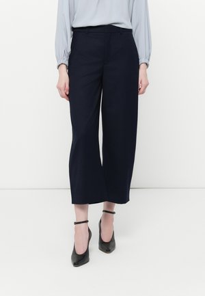 Navy breie benbukser laget av et glatt stoff, med en skreddersydd midje. Kombinert med svarte ankelrem-sandaler for kontrast.