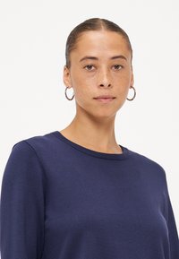 Maglione girocollo blu navy con maniche lunghe, texture liscia e dettagli lavorati a maglia discreti. Presenta una vestibilità rilassata e collo a coste.