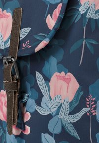 Květinový batoh s tmavě modrým pozadím, růžovými pivonkami a zelenými listy. Obsahuje tmavě hnědý kožený popruh a kovovou sponu.