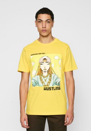 Rumena bombažna majica s kratkimi rokavi, ki vsebuje grafični odtis lika z dolgimi lasmi in dodatki, pod podobo pa je napis "HUSTLING".