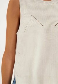 Pull en tricot léger de couleur blanc cassé, avec une texture côtelée, un col rond et des motifs décoratifs subtils à l'avant.