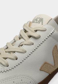 Baskets blanches en cuir texturé, accents beiges, bout rond et lacets plats. Présente le logo "Veja" sur la languette et une semelle en caoutchouc.