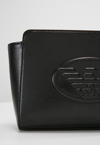 Borsa a mano in pelle nera con finitura testurizzata, caratterizzata da un design del logo impresso e una forma strutturata. Aspetto minimalista e raffinato.